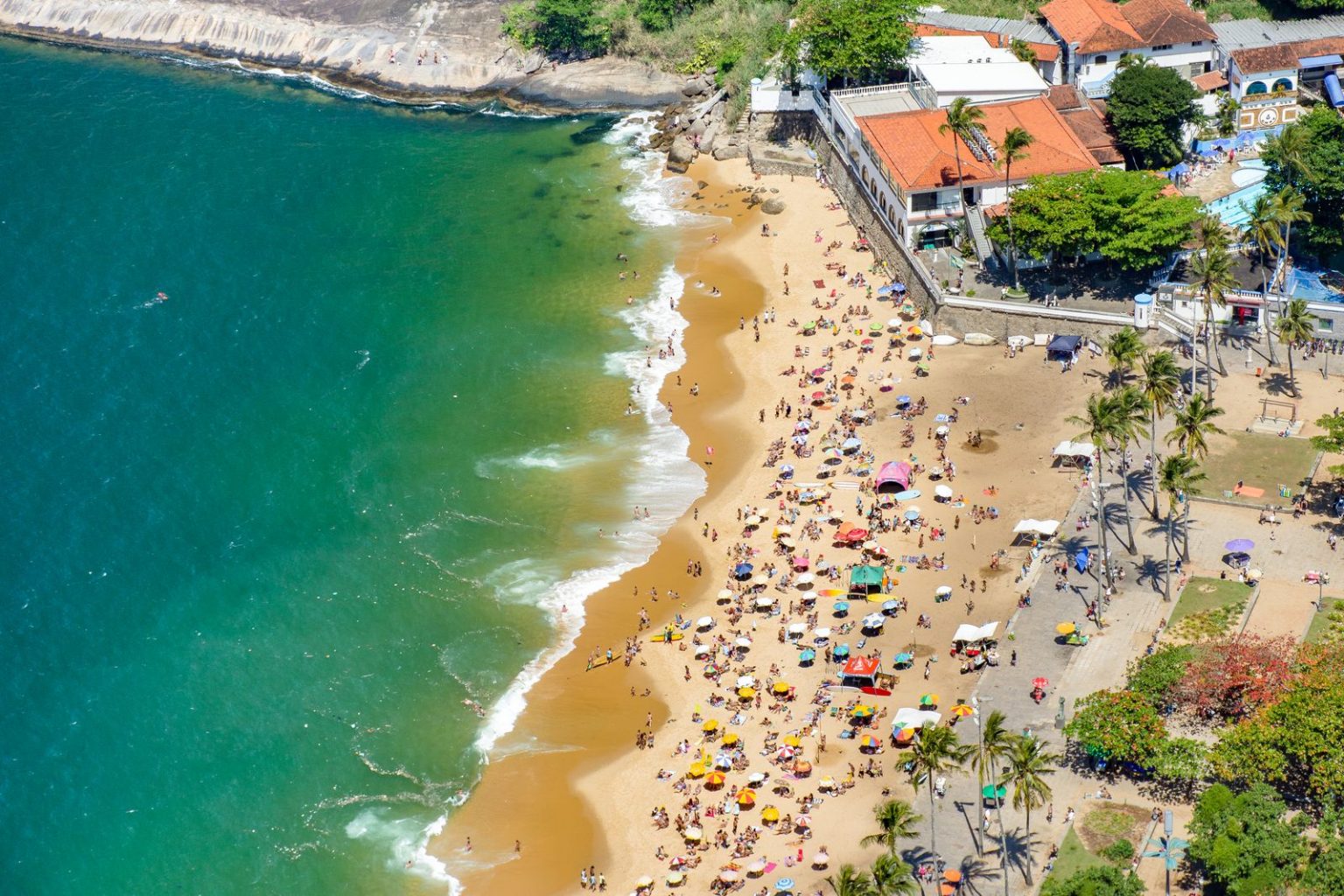 Aerial view of a busy beach in Rio de Janeiro, Brazil, with umbrellas and palm trees