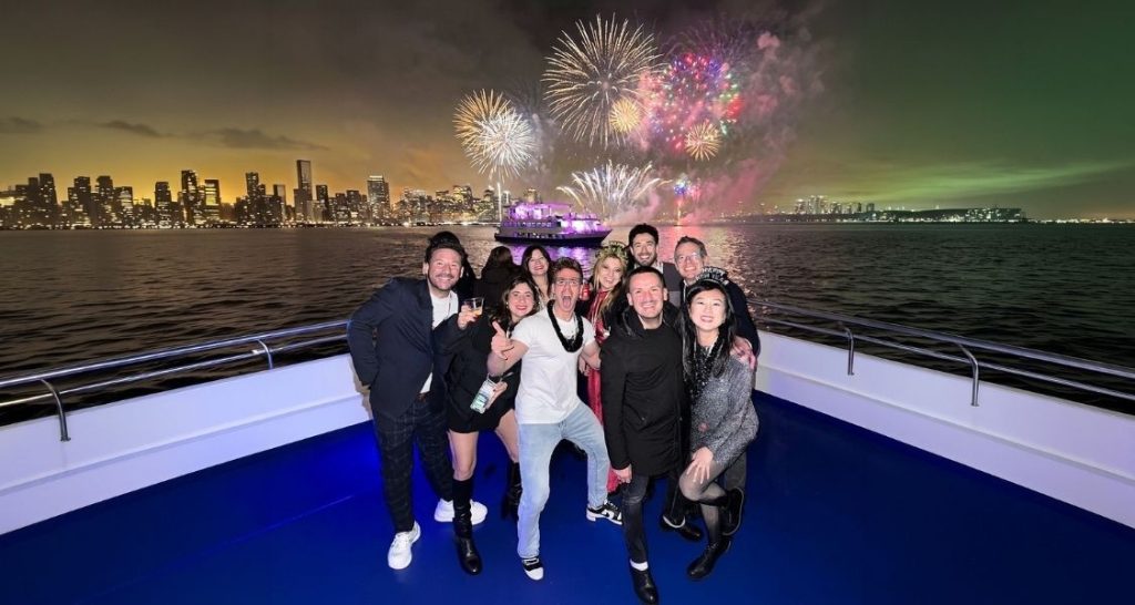 WeRoad group of solo travellers celebrating New Year on a boat with fireworks over the New York skyline