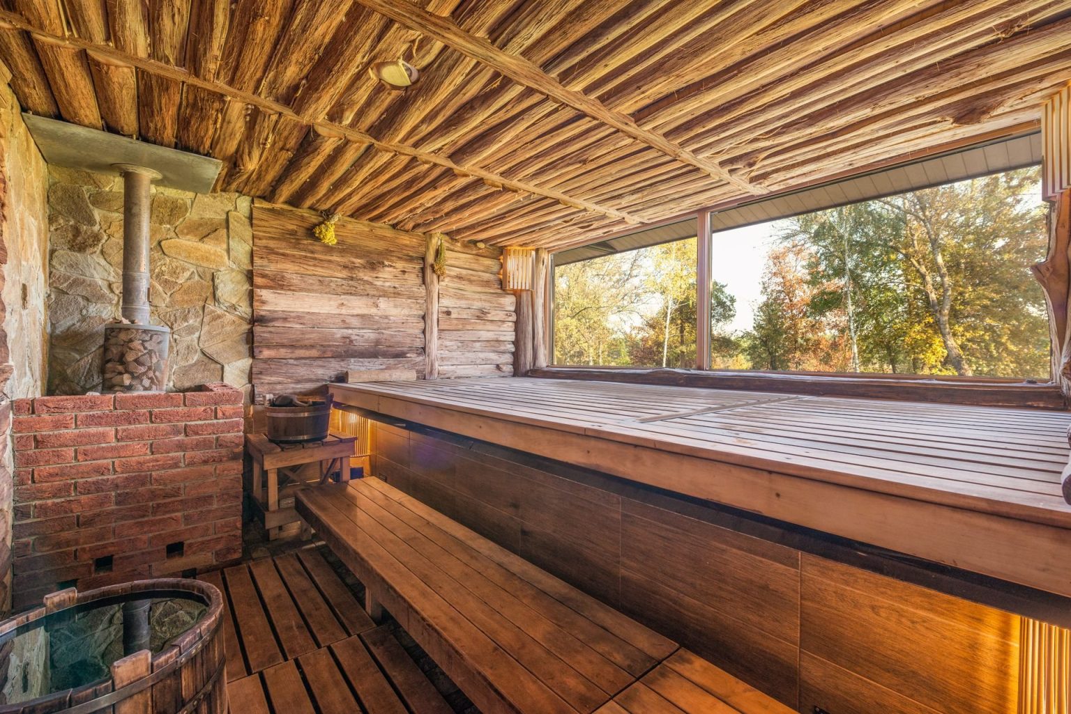 A rustic wooden sauna with a wide window looking out onto trees
